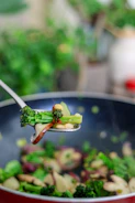 Close-up of a sturdy metal scoop and a frying pan with fresh vegetables inside.