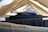 A close-up view of multiple pairs of trousers hanging on wooden hangers, arranged in a row. The hangers are spaced evenly, displaying a range of dark and neutral colors such as black, navy, and brown.