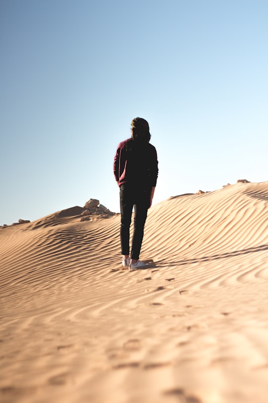 man in black jacket walking on desert during daytime in Biskra Algeria