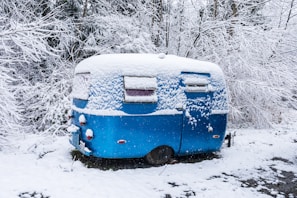 A custom flatbed camper parked beside a snowy mountain, showcasing its sturdy build and insulated windows.