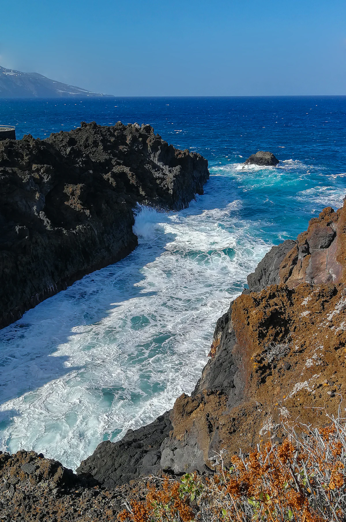 Surf breaking into a cove between dark lava cliffs on the coast of La Palma