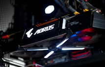 A close-up view of a high-performance graphics card inside a computer, featuring prominent branding and illuminated components. The cables and surrounding hardware components are partially visible, contributing to a sleek, modern tech aesthetic.