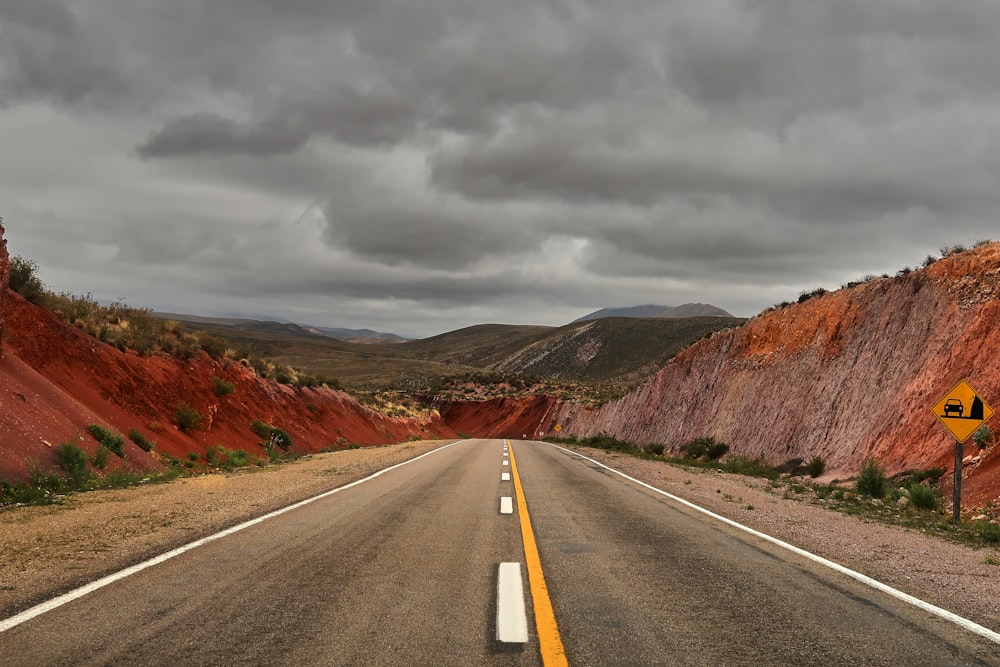 gray concrete road between brown mountains under gray clouds during daytime