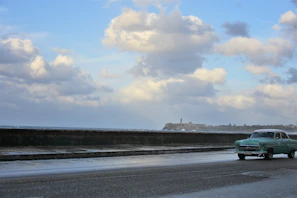 A convoy of elegant cars driving along a scenic coastal highway under clear blue skies