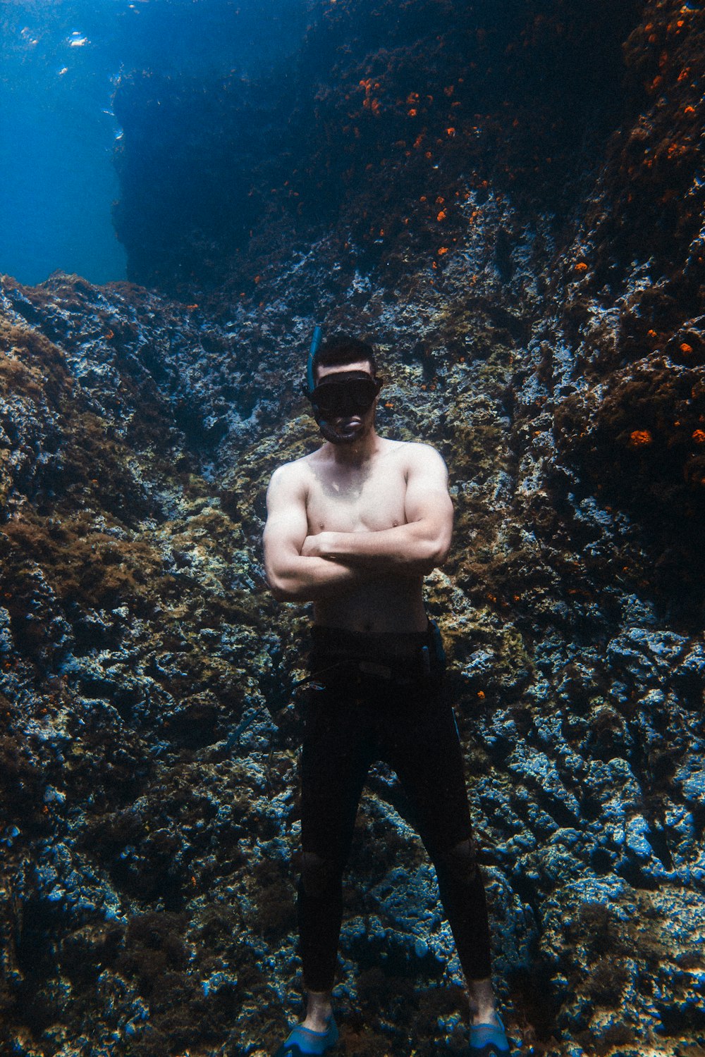 topless man in black pants wearing black cap standing on brown rock