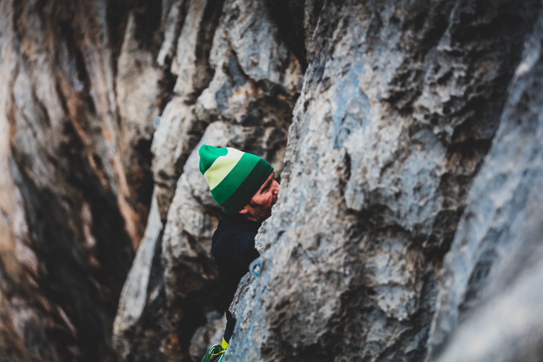 man in green and white hat climbing on gray rock