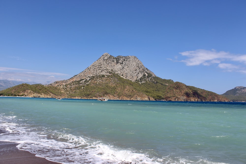 green and brown mountain beside blue sea under blue sky during daytime