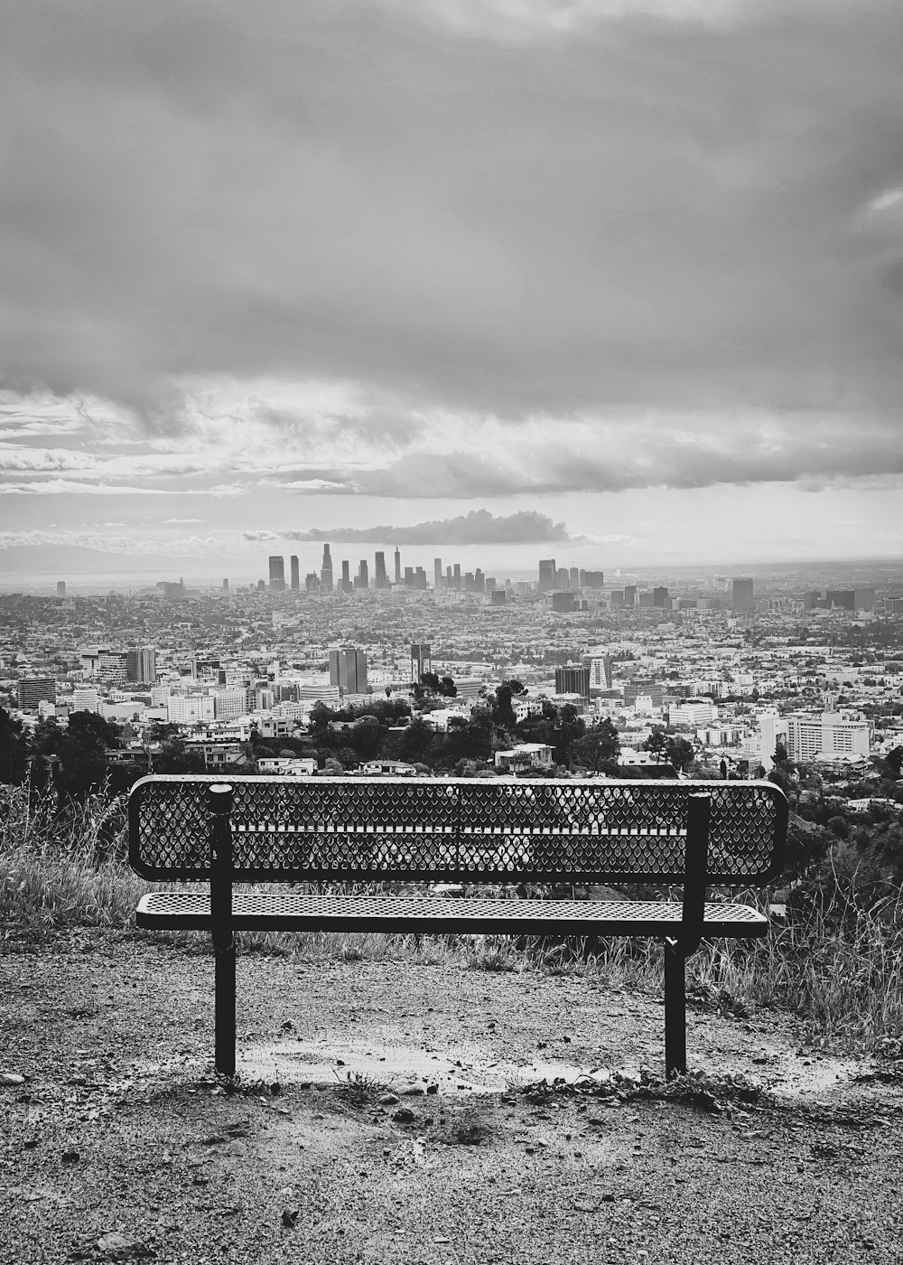 grayscale photo of bench near city buildings