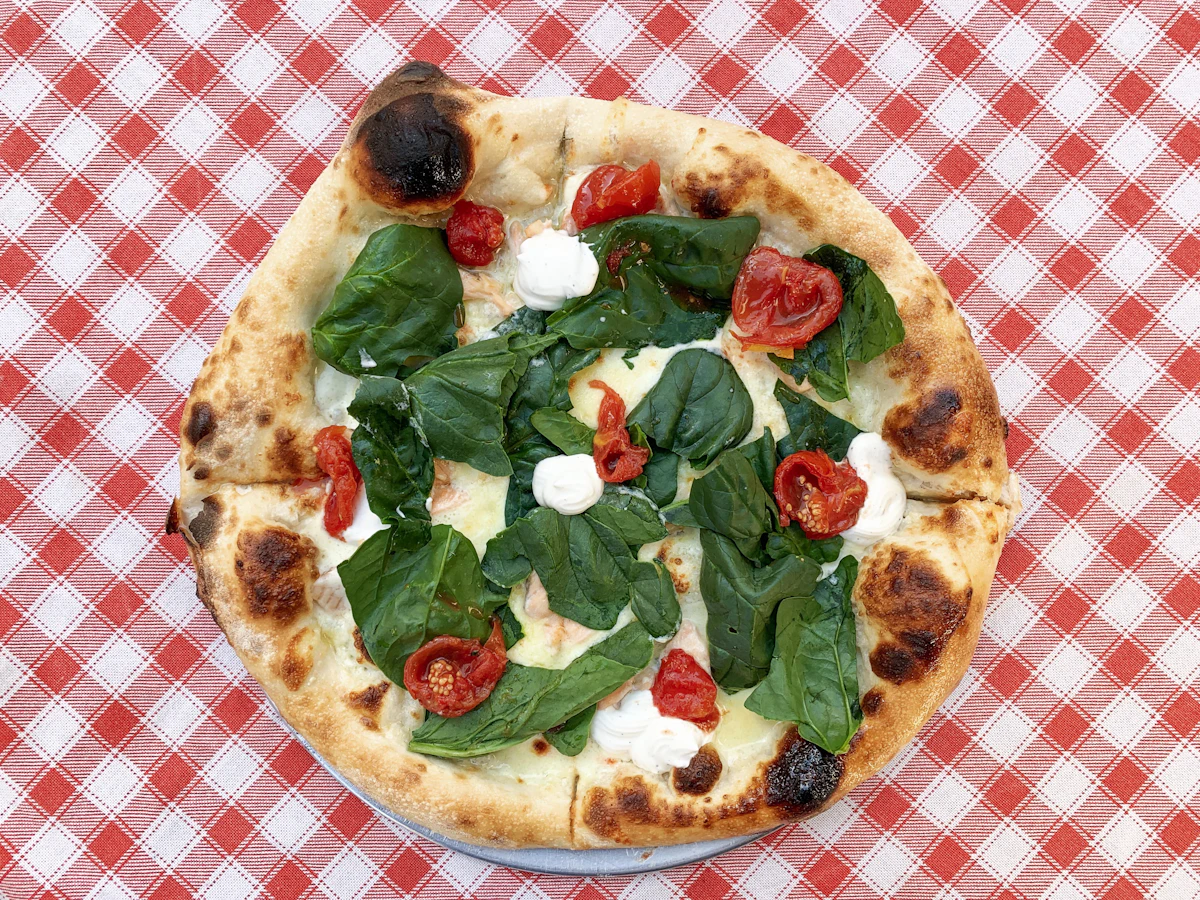 Pizza aux épinards, tomates cerises et mozzarella, vue du dessus sur une nappe à carreaux rouges et blancs