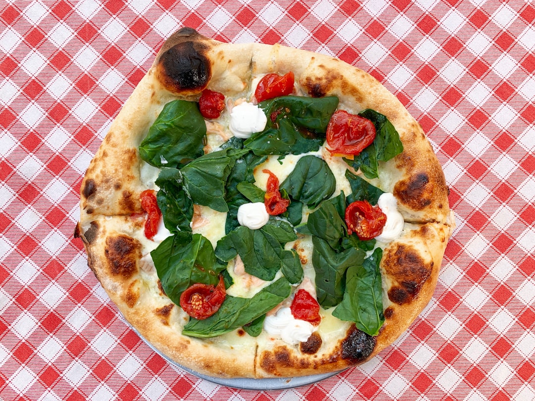 Delicious Italian pizza with spinach, cherry tomatoes, cream cheese and mozarella on checked Italian tablecloth