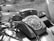 A vintage rotary dial telephone is placed on a reflective surface with some leaves partially covering it. The scene seems to be indoors, possibly by a window, as natural light casts shadows on the phone and surrounding objects.