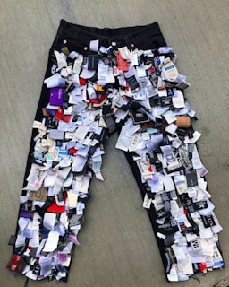 A pair of jeans is covered in numerous clothing tags and labels, creating a textured, layered effect. The jeans are laid out on a flat surface, showcasing a variety of colors and text on the tags.