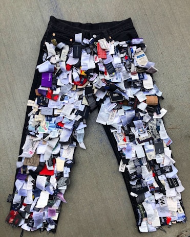 A pair of jeans is covered in numerous clothing tags and labels, creating a textured, layered effect. The jeans are laid out on a flat surface, showcasing a variety of colors and text on the tags.