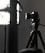 A professional camera is mounted on a tripod, positioned next to a large, soft light diffuser. The scene presents a typical photography studio setup, with focus on the camera equipment and lighting.