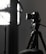 A professional camera is mounted on a tripod, positioned next to a large, soft light diffuser. The scene presents a typical photography studio setup, with focus on the camera equipment and lighting.