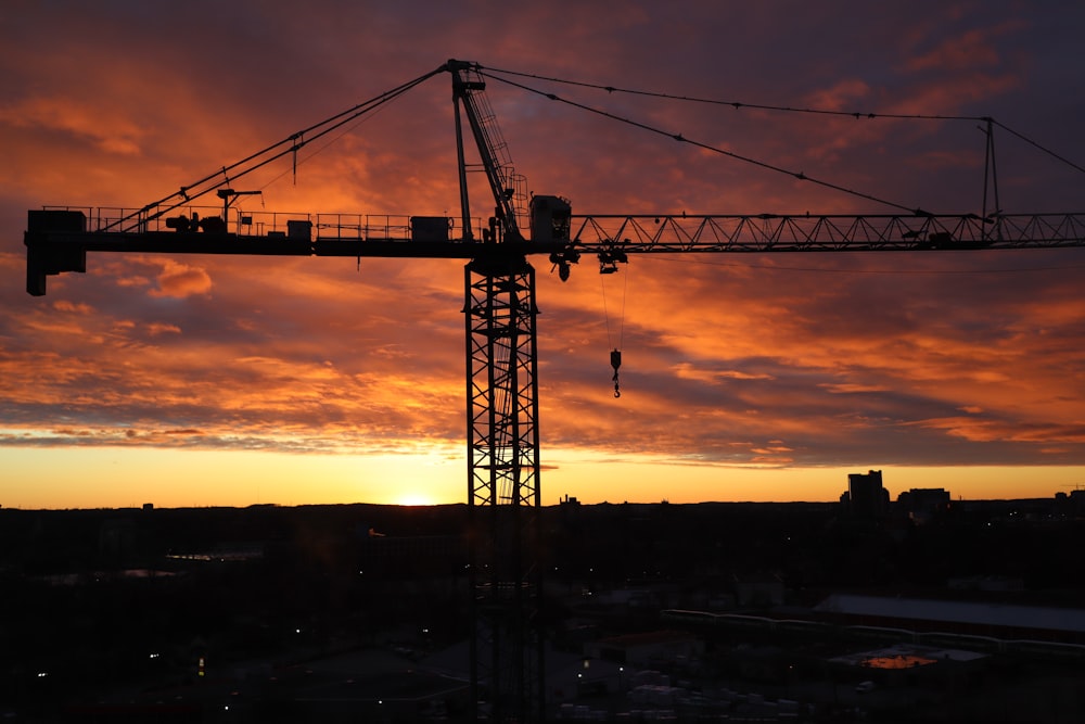 silhouette of crane under orange and gray cloudy sky during sunset
