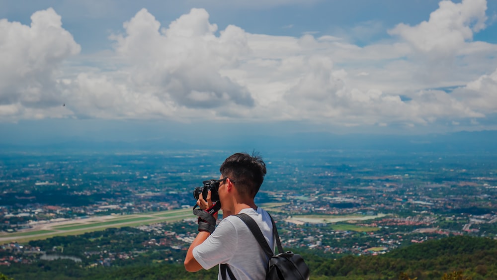 man in white t-shirt taking photo of green mountains during daytime