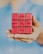 A hand holding a modified Rubik's Cube with red faces, each block displaying words. The words 'FIGURE IT OUT' are arranged in a sequence across the front of the cube. The background is softly blurred, highlighting the cube.