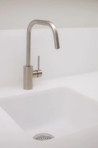 A sleek kitchen sink and faucet setup with matching sanitary fixtures in a bright, modern utility space.