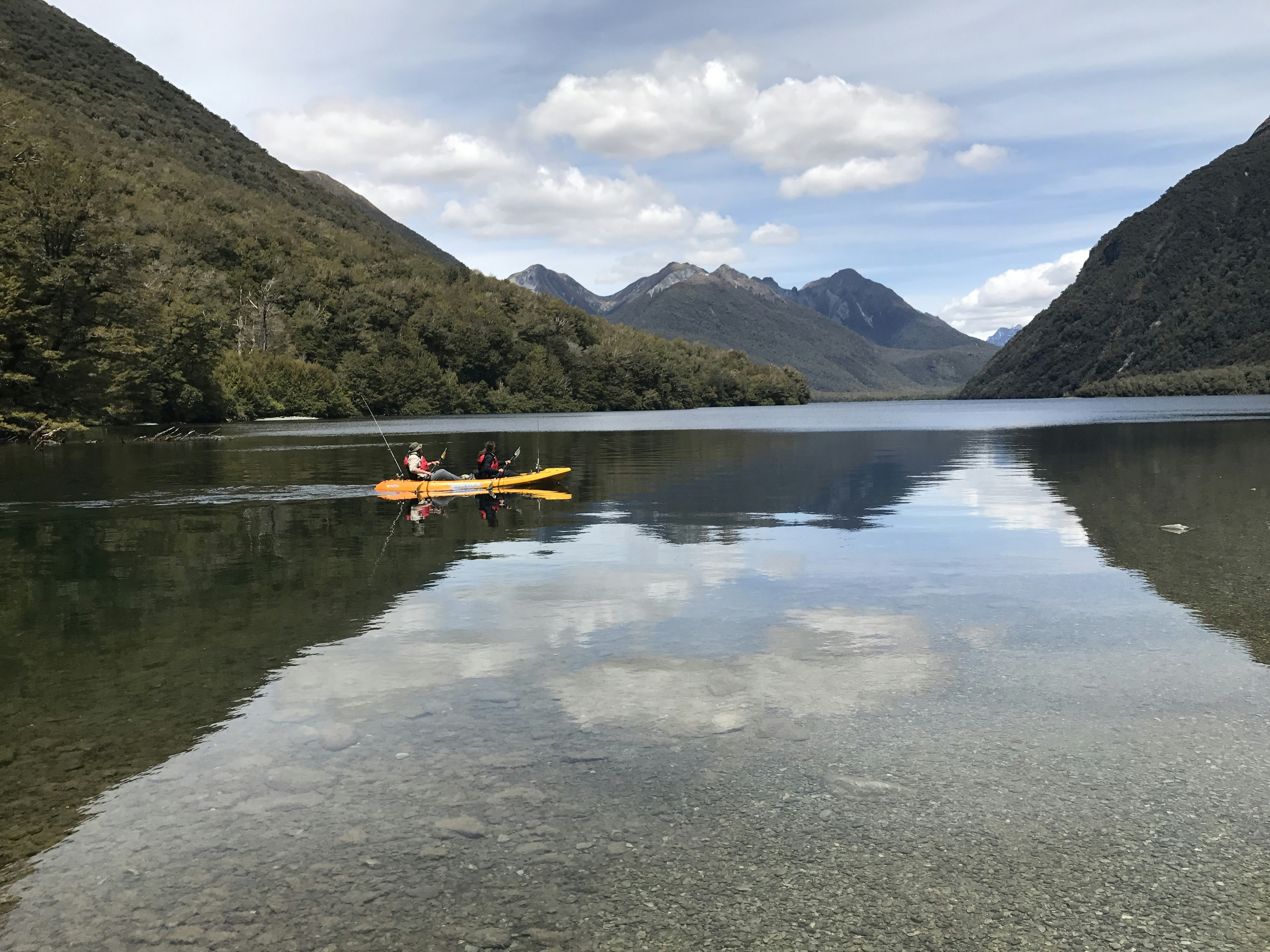 orang yang mengendarai kayak oranye di danau pada siang hari