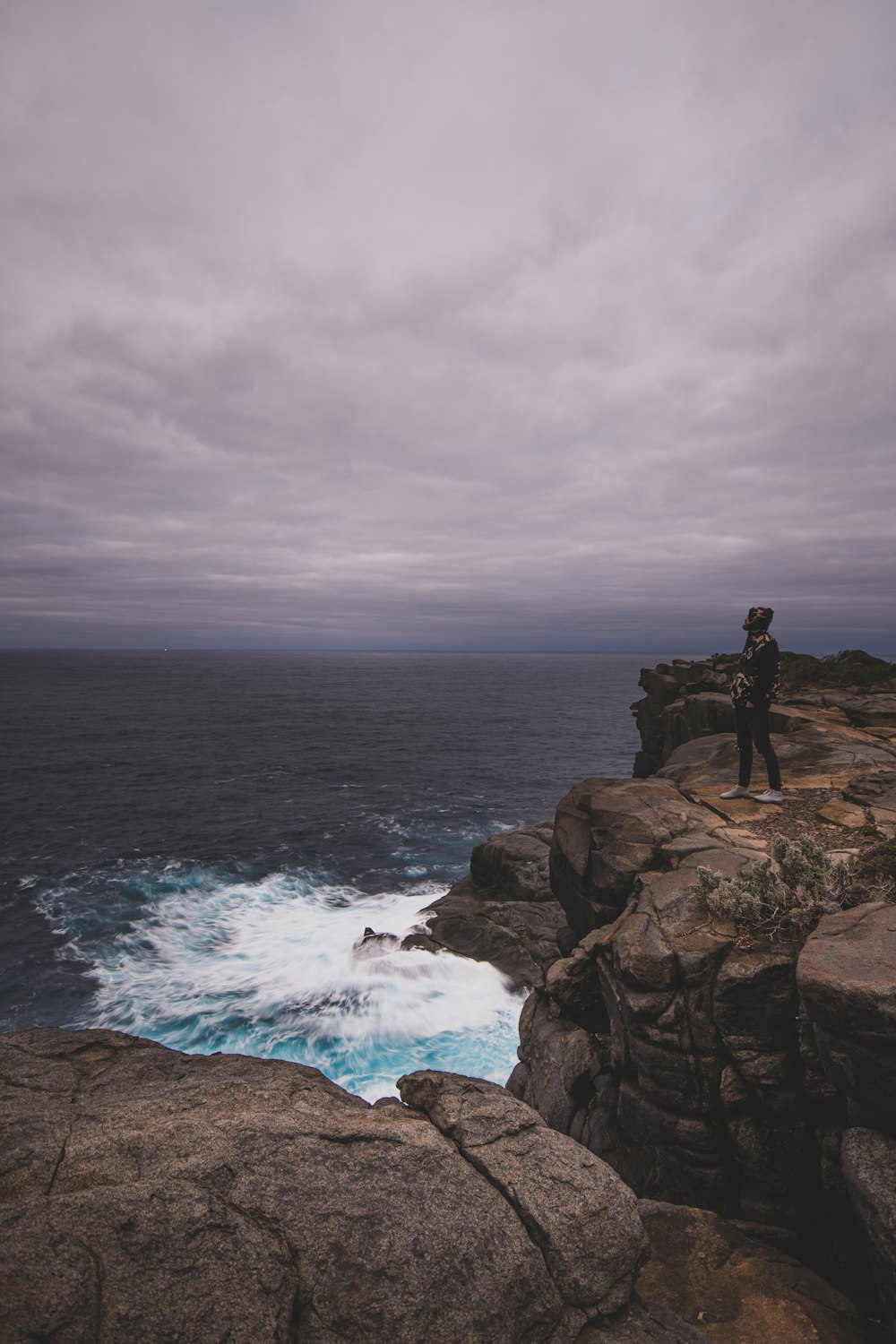 man standing on rock formation near sea during daytime