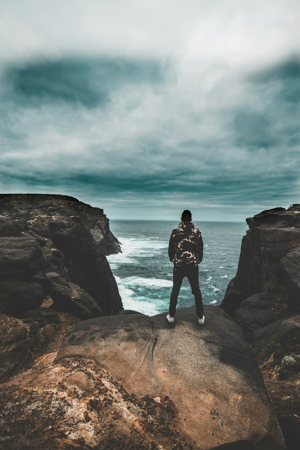 woman in black dress standing on rock formation near body of water during daytime