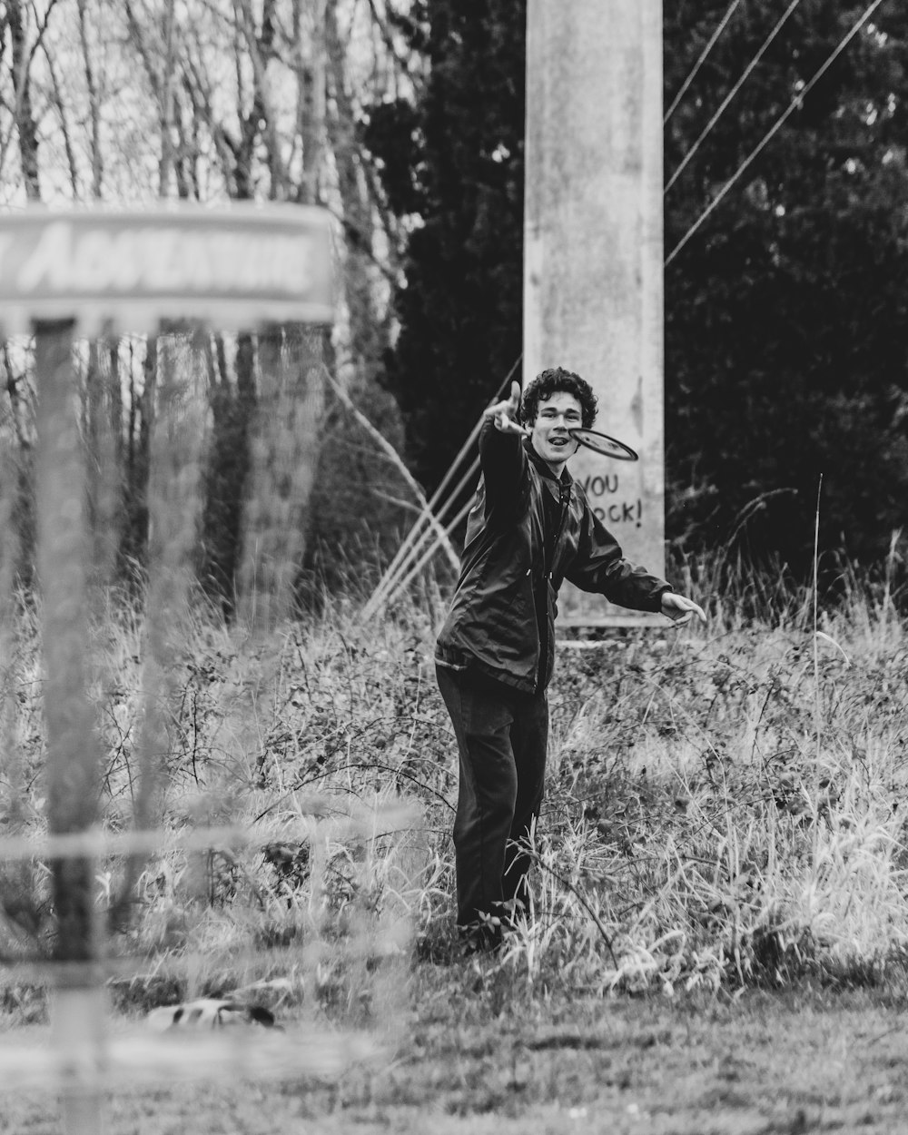 uomo in giacca e pantaloni neri in piedi accanto al palo concreto nella fotografia in scala di grigi