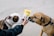 Two dogs are shown sniffing a packet labeled CBD pet chews held by a person. The dogs are wearing collars and leashes, and one of the dogs is brown with a black collar while the other is a mix of white and brown with a pink collar. The background is a gray pavement.