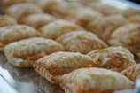 A tray filled with several golden-brown, flaky pastries placed in rows. The pastries have a slightly puffed appearance with a visible layered texture.