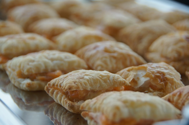 A tray filled with several golden-brown, flaky pastries placed in rows. The pastries have a slightly puffed appearance with a visible layered texture.