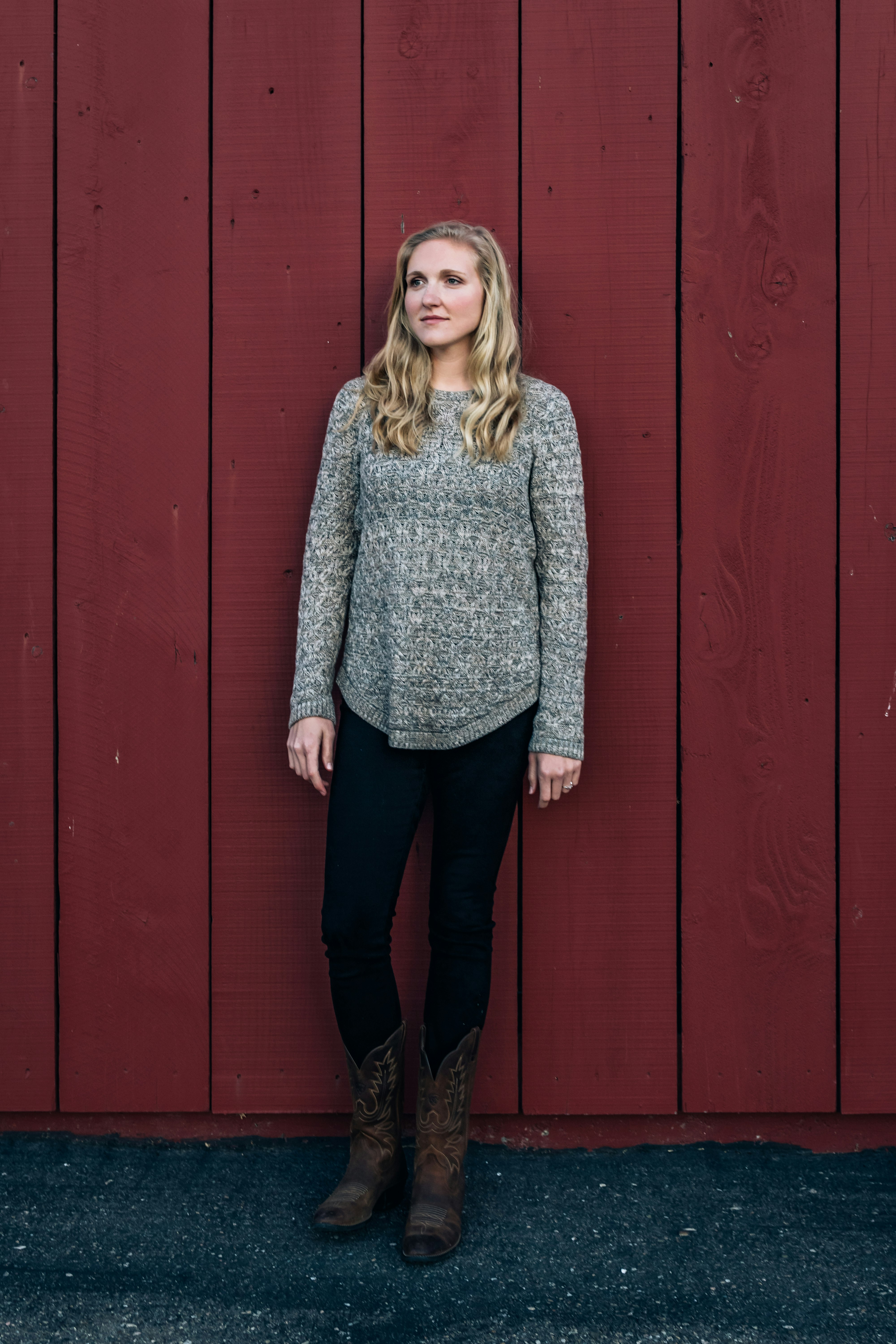 woman in gray sweater standing beside red wooden wall