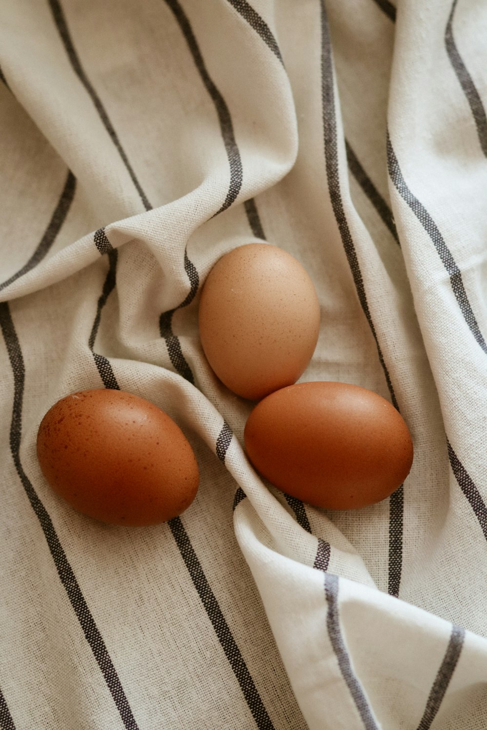 three brown eggs on a white and black striped cloth