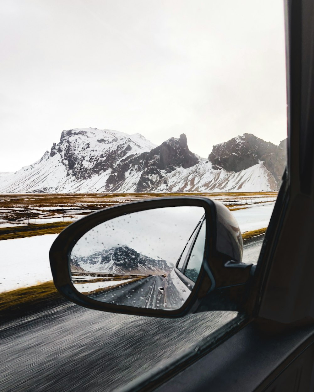 car side mirror with snow covered mountain in the distance