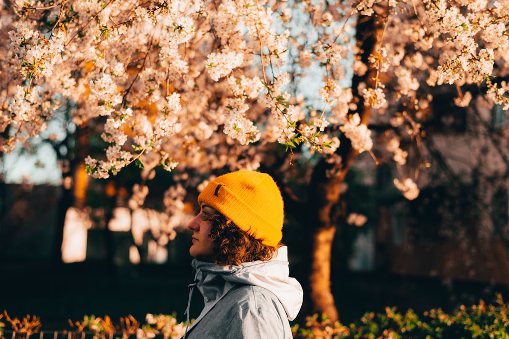 man in yellow knit cap and white jacket standing under white cherry blossom tree during daytime
