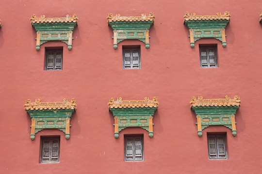 A series of windows with ornate, decorative architectural elements line a red wall. The windows have intricate lattice designs, and above them are detailed cornices painted in green and orange, accented with gold.