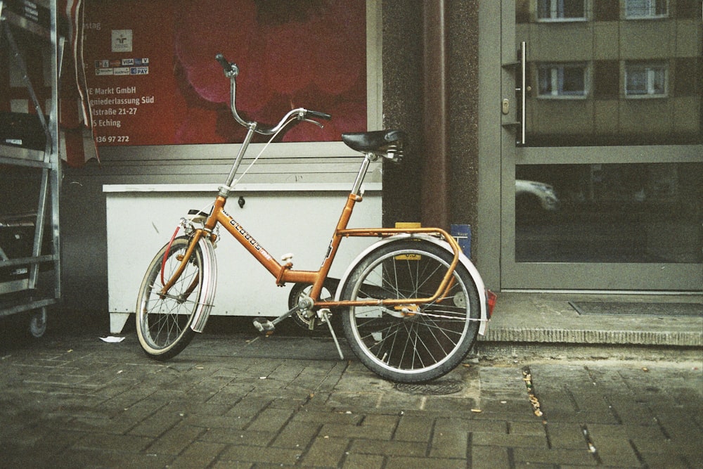 Bicicletta arancione della città parcheggiata accanto all'edificio in cemento marrone