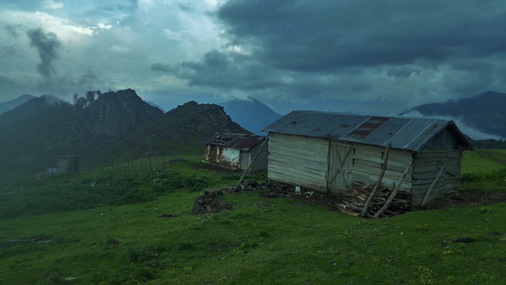 brown wooden house on green grass field near mountain under white clouds during daytime