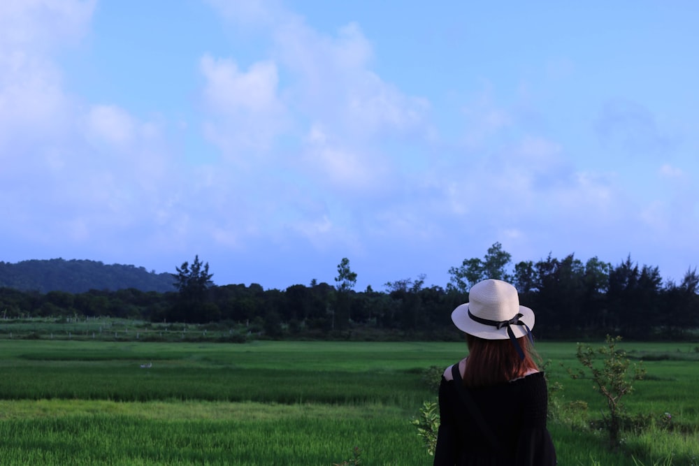 woman in brown shirt wearing white hat standing on green grass field under white clouds and