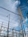 High voltage electrical transmission towers and power lines dominate the scene against a partly cloudy blue sky. Various metal structures and a streetlight are also visible, forming part of an electrical substation.