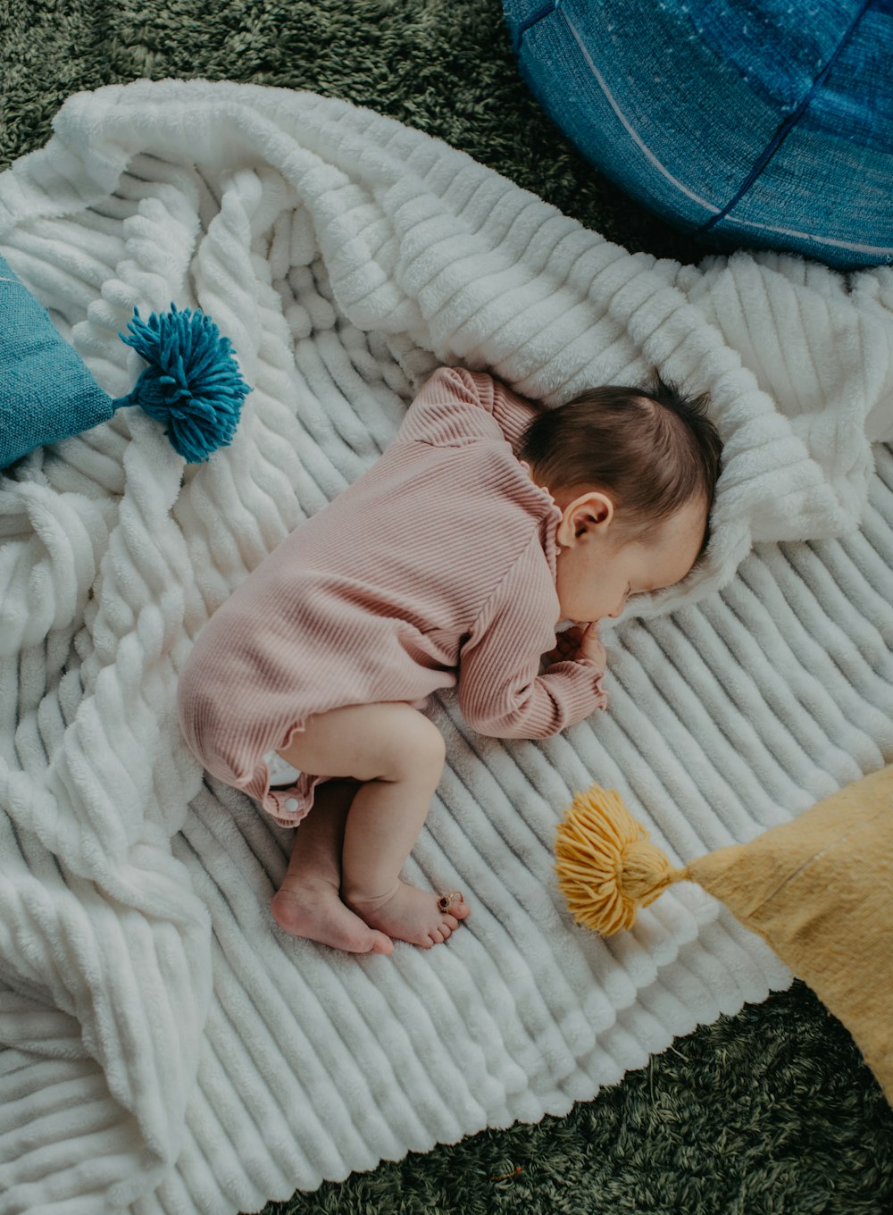 Baby in rosa Onesie liegt auf weißem Bett