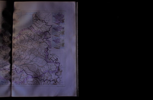 A detailed map is partially visible, showing geographic features and potential roads or borders marked with lines. The map covers a region with intricate details, including various insets or smaller maps in the top right corner. The left side is dimly lit, adding a shadowy effect.
