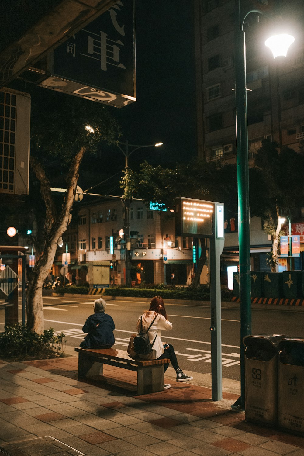 man and woman sitting on bench near street light during night time