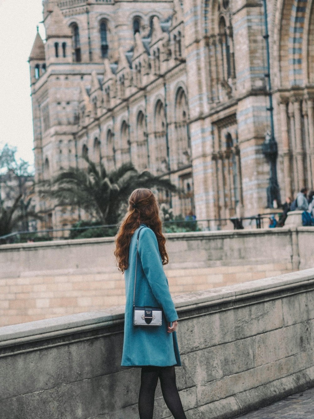 woman in blue coat standing on gray concrete stairs during daytime