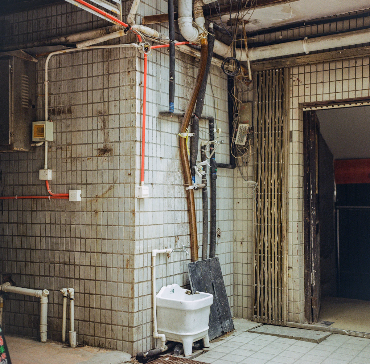 An old tiled basement utility room with a laundry sink and exposed pipes