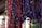 Multiple strands of handcrafted paper beads in various colors, primarily red, purple, and yellow, hang in vertical rows. The beads are textured and cylindrical in shape, with a natural and artisanal appearance. The background is softly focused, emphasizing the vibrant colors and craftsmanship of the beads.