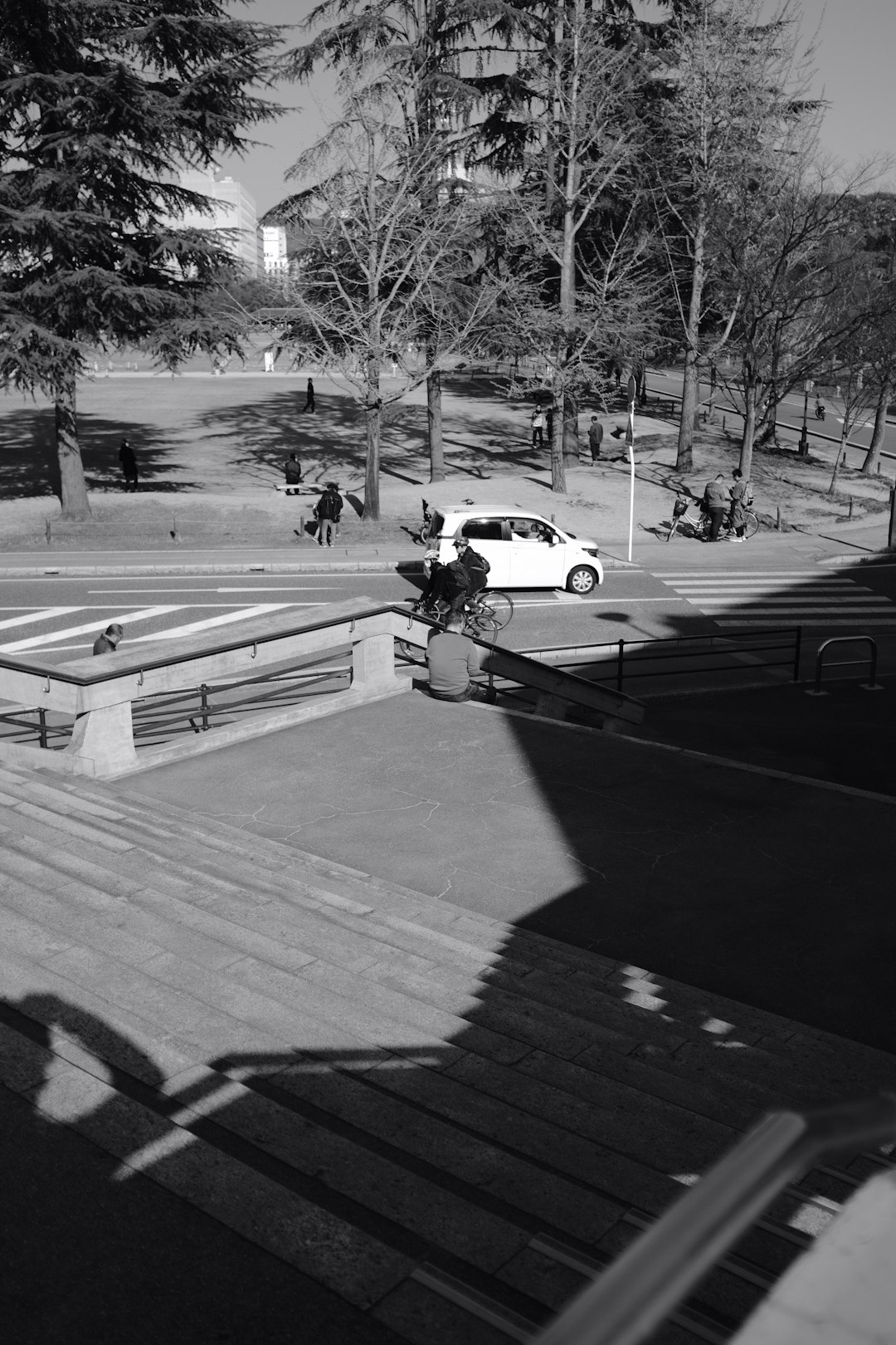 grayscale photo of man in black jacket and pants walking on sidewalk