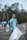 A group of people wearing blue T-shirts with the words 'Ocean Cleanup Group' engaged in a beach cleanup. They are holding large white garbage bags to collect trash. The background features trees and a cloudy sky, creating a natural environment.