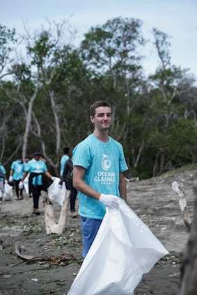 A diverse group of volunteers planting trees along a coastal shoreline under a bright blue sky.