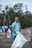 A group of people wearing blue T-shirts with the words 'Ocean Cleanup Group' engaged in a beach cleanup. They are holding large white garbage bags to collect trash. The background features trees and a cloudy sky, creating a natural environment.