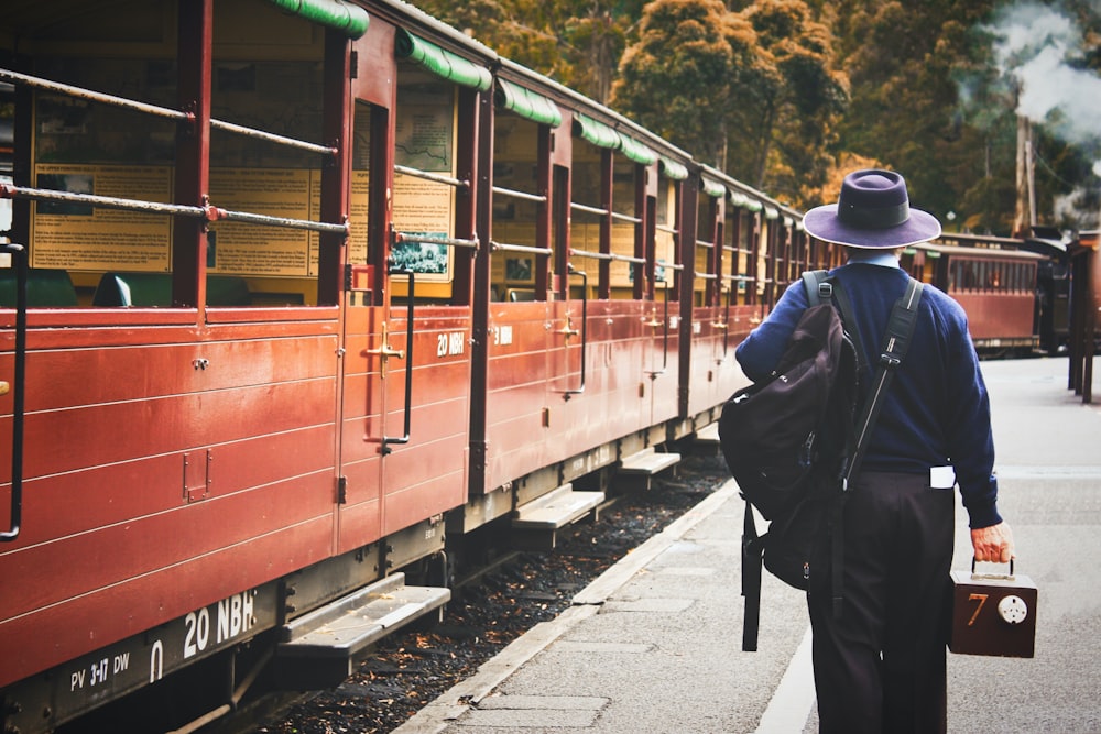 homem em jaqueta preta e chapéu preto de pé ao lado do trem vermelho durante o dia